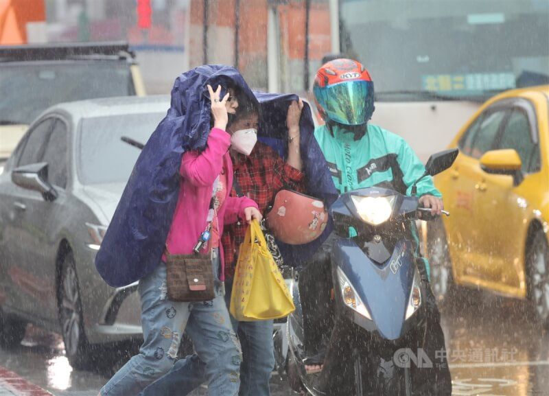 中央氣象署預報，5日起鋒面接近，各地易有短暫陣雨或雷雨。圖為台北市信義區街頭民眾以雨衣遮擋雨勢。（中央社檔案照片）